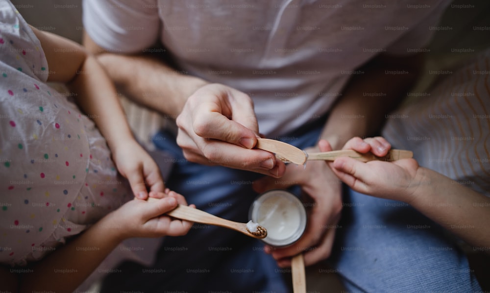 Une vue de dessus des mains d’un père méconnaissable avec deux jeunes enfants se brossant les dents à l’intérieur à la maison, concept de style de vie durable.