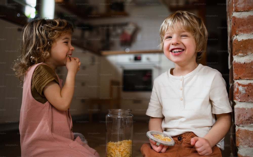 2人の小さな子供が家の屋内で、床でコーンフレークを食べています。