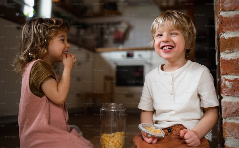 Two small children indoors at home, eating cornflakes on floor.