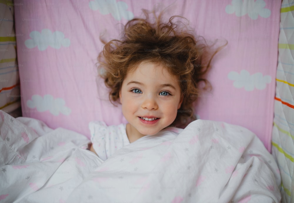 Ein Porträt eines niedlichen kleinen Mädchens, das zu Hause im Bett liegt und in die Kamera schaut.