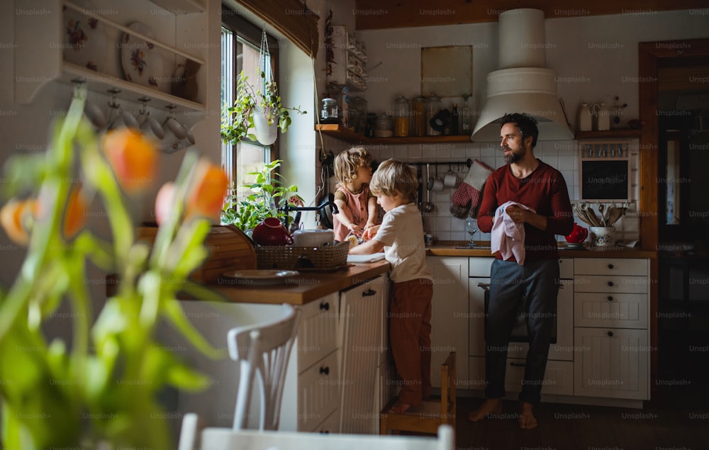 Un père d’âge mûr avec deux jeunes enfants qui font la vaisselle à l’intérieur à la maison, concept de tâches quotidiennes.