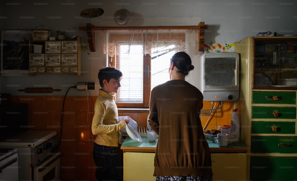 Porträt einer armen, reifen Mutter und einer kleinen Tochter, die zu Hause drinnen Geschirr spülen, Armutskonzept.