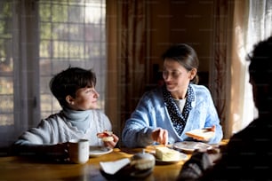 A portrait of happy poor sad small girl with parents eating indoors at home, poverty concept.