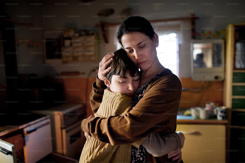Ein Porträt einer traurigen, armen, reifen Mutter, die ihre kleine Tochter zu Hause umarmt, Armutskonzept.
