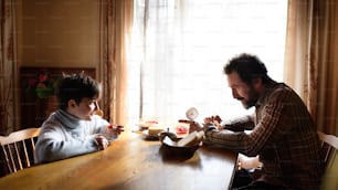 Ein Porträt eines armen kleinen Mädchens mit Vater, der zu Hause drinnen isst, Armutskonzept.
