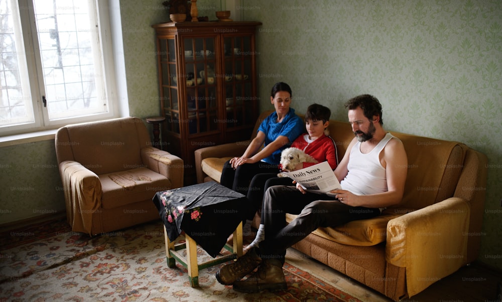 Portrait of poor mature couple with small daughter indoors on sofa at home, poverty concept.