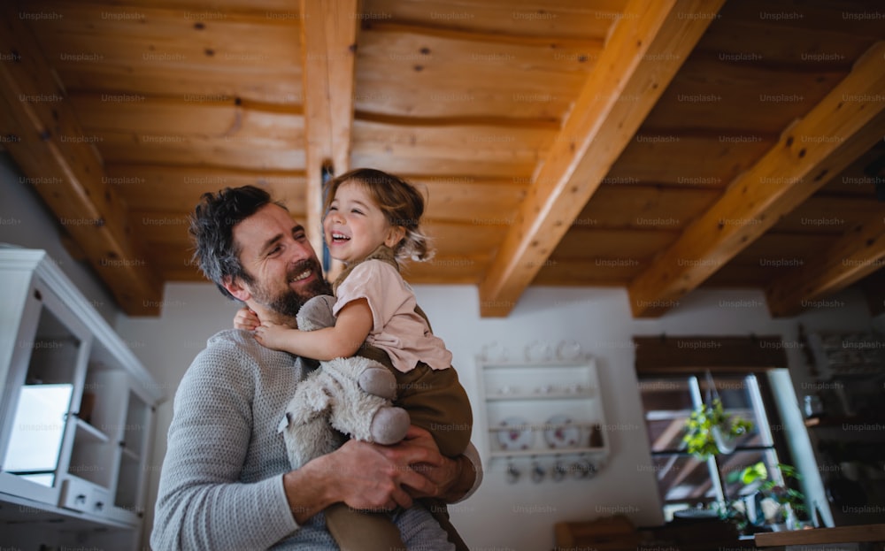 A low angle view of mature father with small daughter having fun indoors at home, holding and hugging.