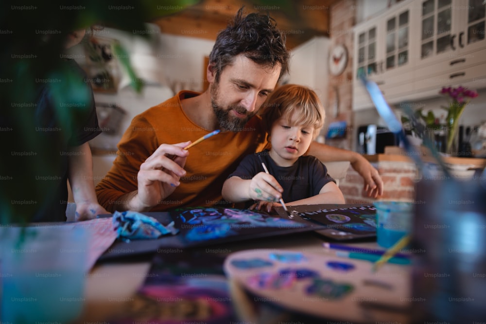 Ein reifer Vater mit zwei kleinen Kindern, der sich zu Hause ausruht und Bilder malt.
