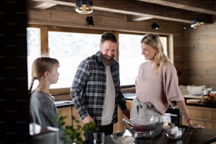 Famille heureuse avec petite fille cuisinant à l’intérieur, vacances d’hiver dans un appartement privé.