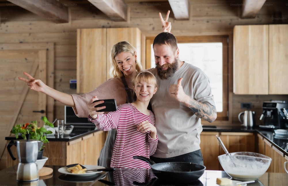 Eine Familie mit kleiner Tochter, die Selfie beim Kochen drinnen macht, Winterurlaub in einer privaten Wohnung.