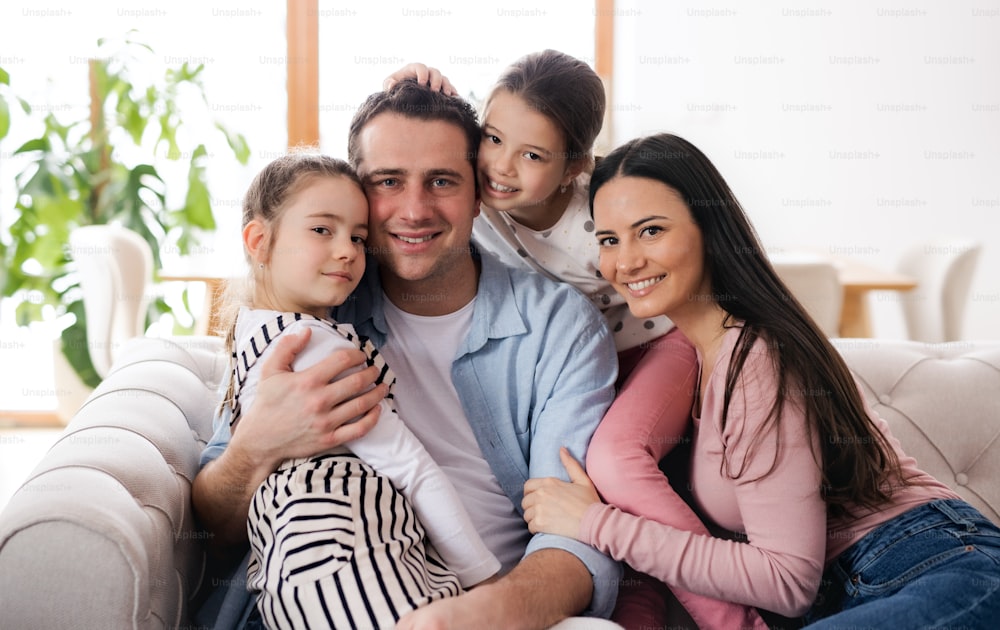 Portrait of parents with small daughters sitting on sofa indoors at home, looking at camera.