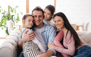 Portrait of parents with small daughters sitting on sofa indoors at home, looking at camera.