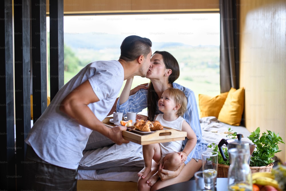 Young family with small daughter kissing indoors, weekend away in container house in countryside.