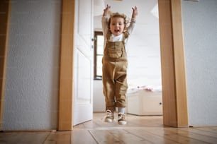 Front view of small toddler girl jumping indoors at home, having fun.
