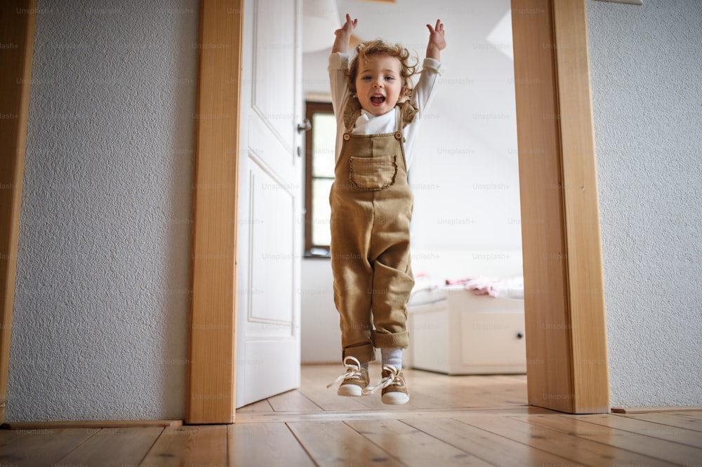 Front view of small toddler girl jumping indoors at home, having fun.