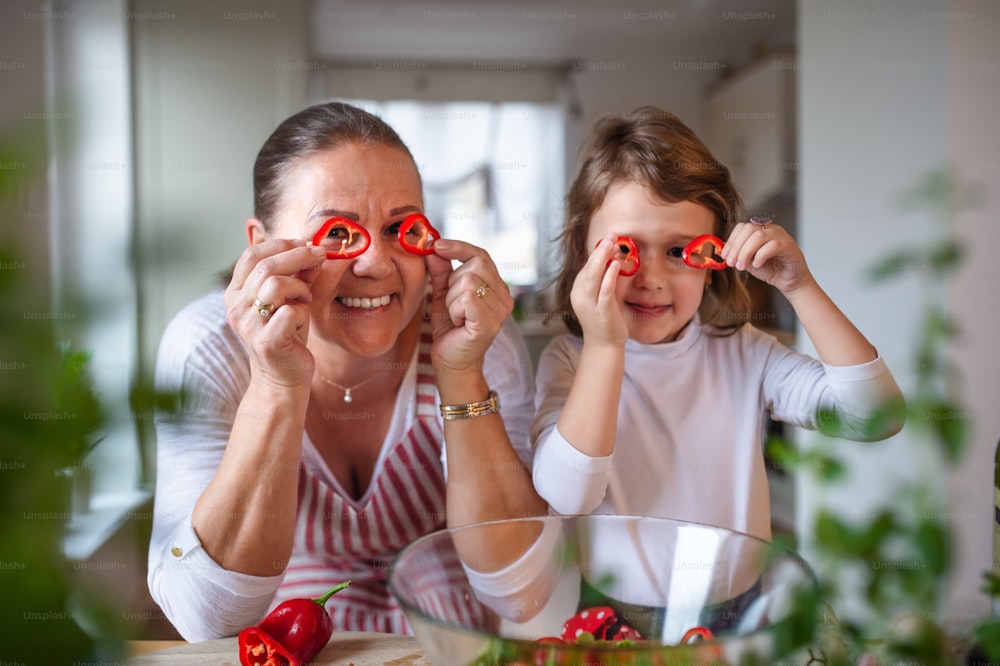 Niña pequeña con abuela mayor en la cocina interior de casa, divirtiéndose cocinando.