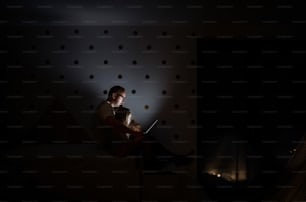 Padre con niños pequeños sentados en el interior en el dormitorio por la noche, usando una computadora portátil.