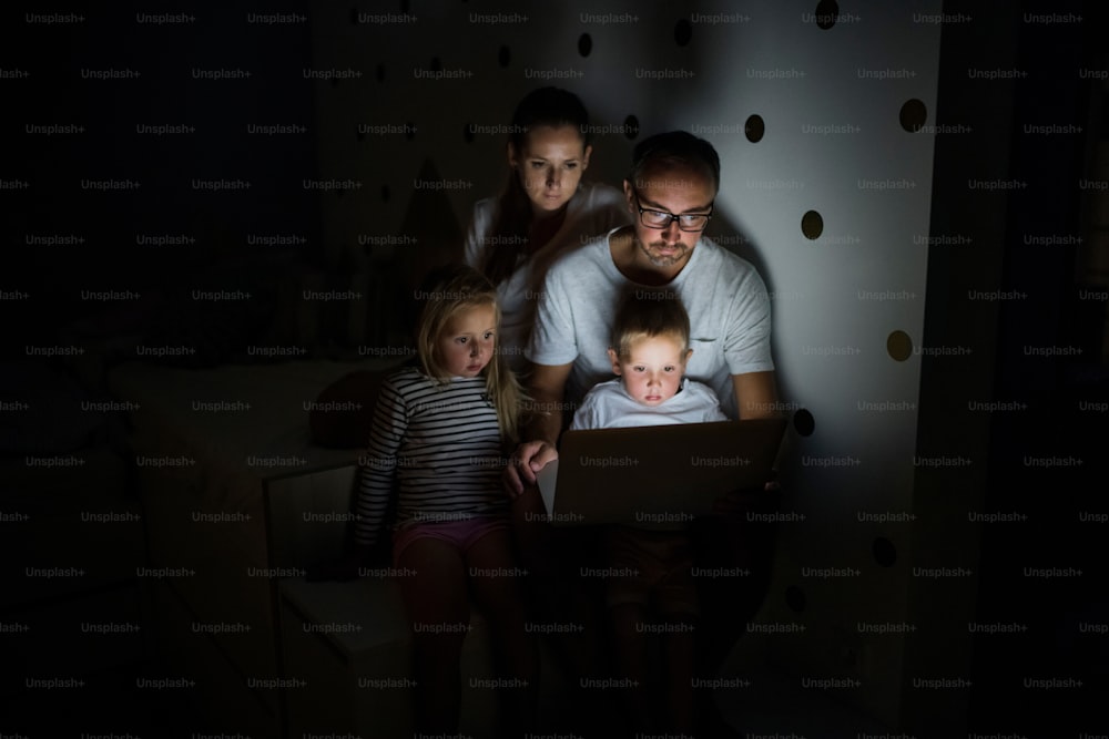 Vista frontal da família com crianças sentadas dentro de casa no quarto, usando laptop.