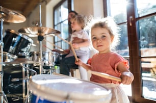 Porträt eines glücklichen kleinen Mädchens drinnen zu Hause, das Schlagzeug spielt.