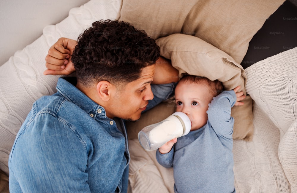 自宅の屋内で、哺乳瓶からミルクを飲む父親と小さな幼児の息子の上面図のポートレート。