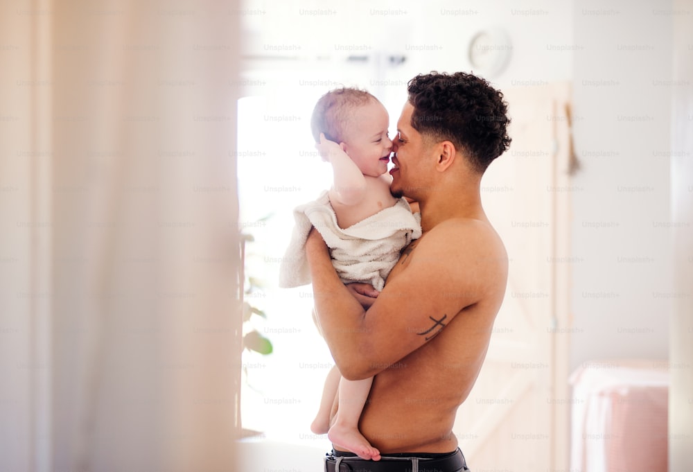 Oben-ohne-Vater und kleiner kleiner Sohn in ein Handtuch gewickelt in einem Badezimmer drinnen zu Hause.