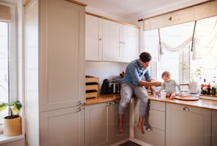 A father and a small toddler son eating fruit and yoghurt in kitchen indoors at home.