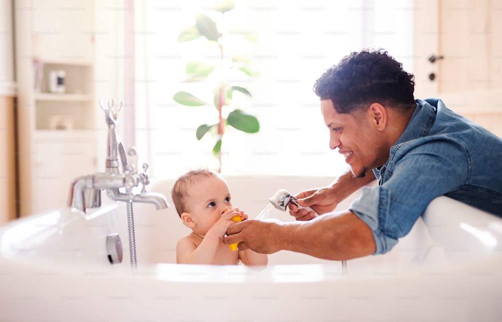 Pai hispânico lavando o filho pequeno em um banheiro dentro de casa.