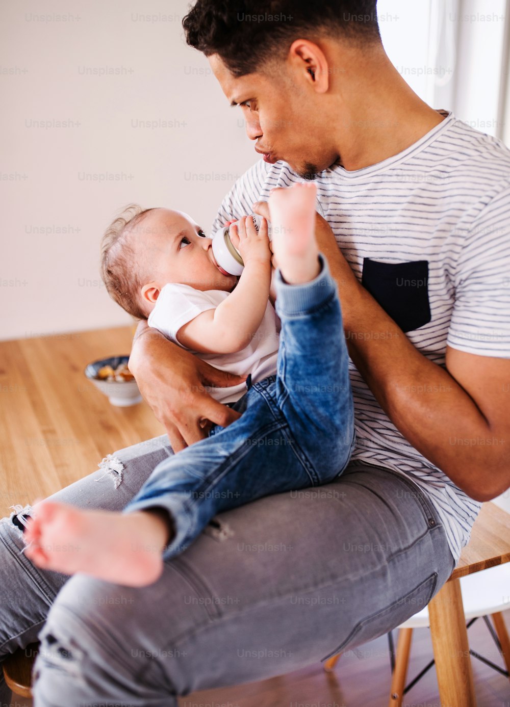 陽気な父親の哺乳瓶が家の屋内で小さな幼児の息子に餌をやるポートレート。