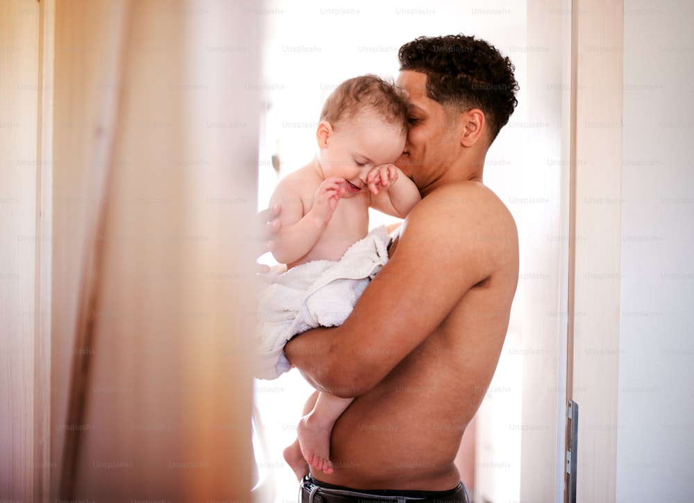 Padre en topless y pequeño hijo pequeño envueltos en una toalla en un baño interior en casa.