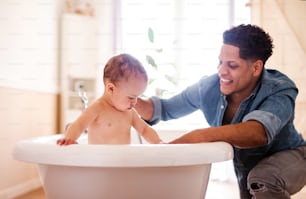 Hispanic father washing small toddler son in a bathroom indoors at home.