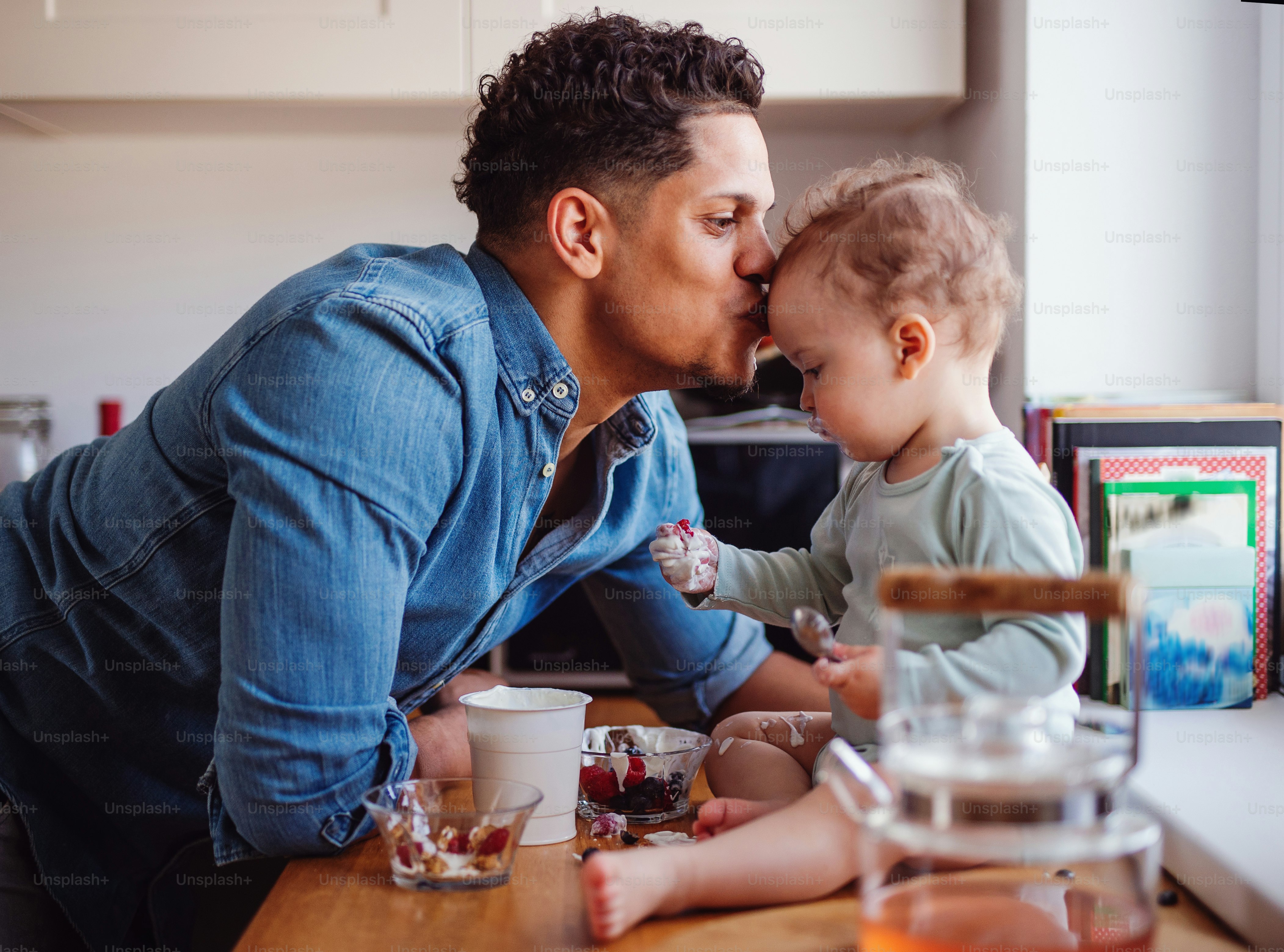A father and a small toddler son eating fruit and yoghurt in kitchen indoors at home
