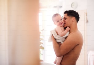 自宅の屋内のバスルームでタオルに包まれたトップレスの父親と小さな幼児の息子。