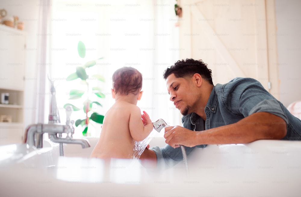 Hispanic father washing small toddler son in a bathroom indoors at home.