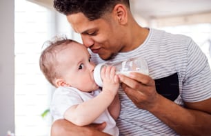 Ein Porträt eines fröhlichen Vaters, der einen kleinen kleinen kleinen Sohn zu Hause mit der Flasche füttert.