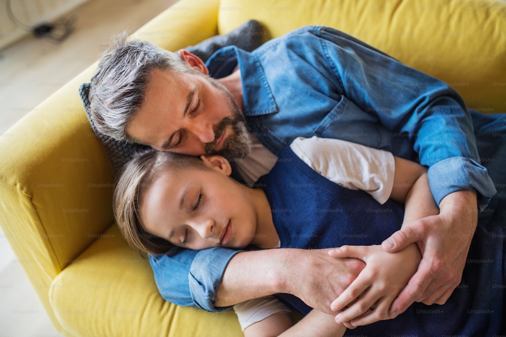 Um pai maduro com filho pequeno deitado no sofá dentro de casa, dormindo e descansando.