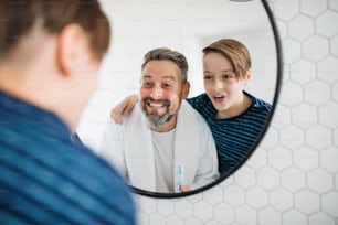 Un padre maduro con un hijo pequeño en el baño por la mañana, cepillándose los dientes.