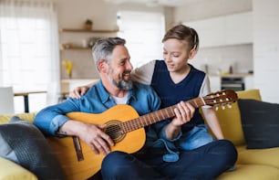 Un padre maturo con un figlio piccolo seduto sul divano in casa, che suona la chitarra.