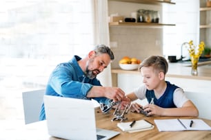 A mature father with small son sitting at table indoors, working on school project.