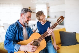 Un padre maturo con un figlio piccolo seduto sul divano in casa, che suona la chitarra.