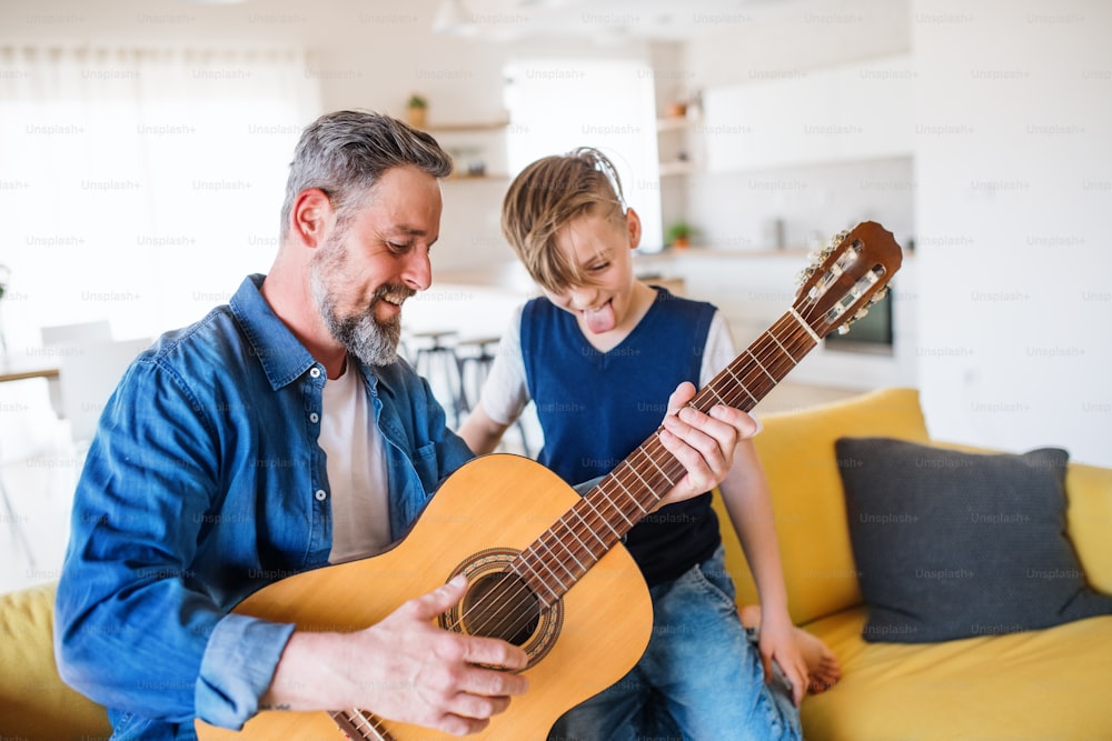 A mature father with small son sitting on sofa indoors, playing guitar..