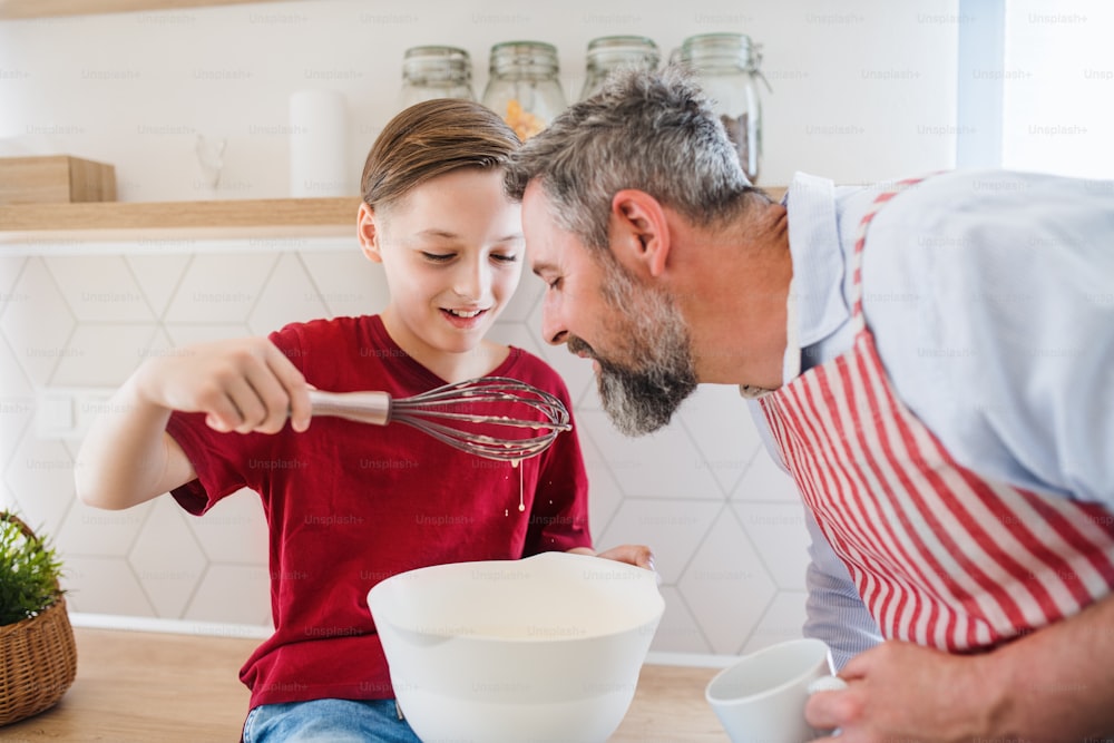 Un père mûr avec un petit fils à l’intérieur dans la cuisine, faisant des crêpes.