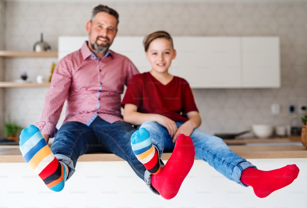 A mature father with small son sitting on kitchen counter indoors, having fun.