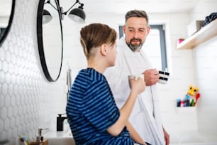 A mature father with small in the bathroom in the morning, holding cups.