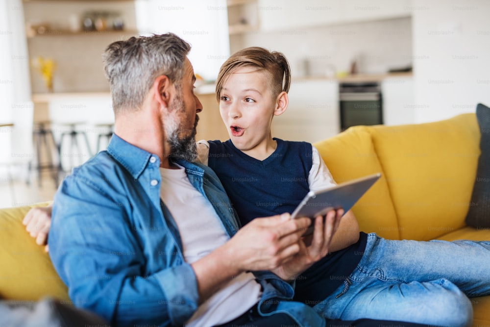 Un padre maturo con un figlio piccolo seduto sul divano in casa, usando il tablet.