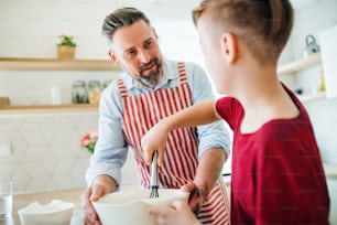 Un padre maturo con un figlio piccolo in casa in cucina, facendo pancake.
