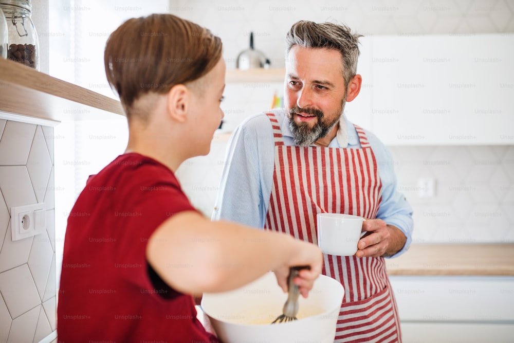 Un padre maturo con un figlio piccolo in casa in cucina, facendo pancake.
