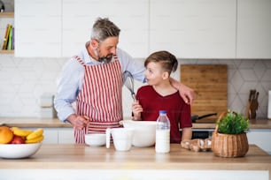 Ein reifer Vater mit kleinem Sohn drinnen in der Küche, der Pfannkuchen macht.