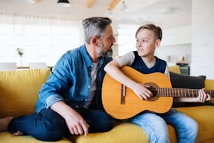 Un padre maduro con un hijo pequeño sentado en el sofá del interior, tocando la guitarra.