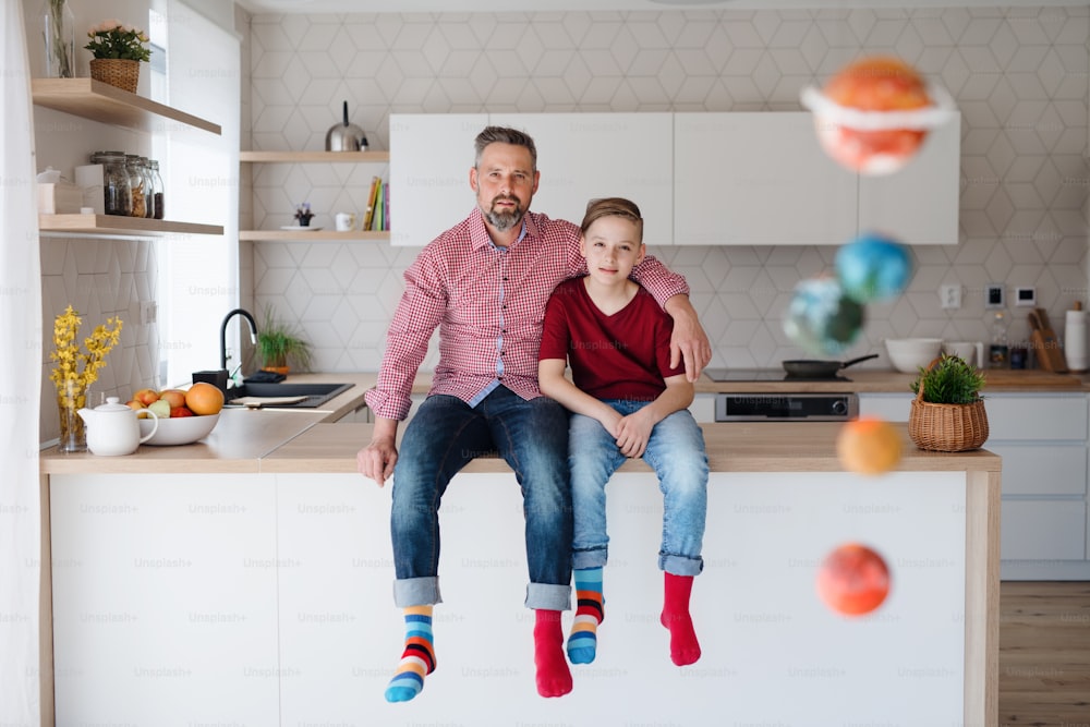 Père mûr et petit fils avec des chaussettes colorées assis sur le comptoir de la cuisine à l’intérieur, regardant la caméra.