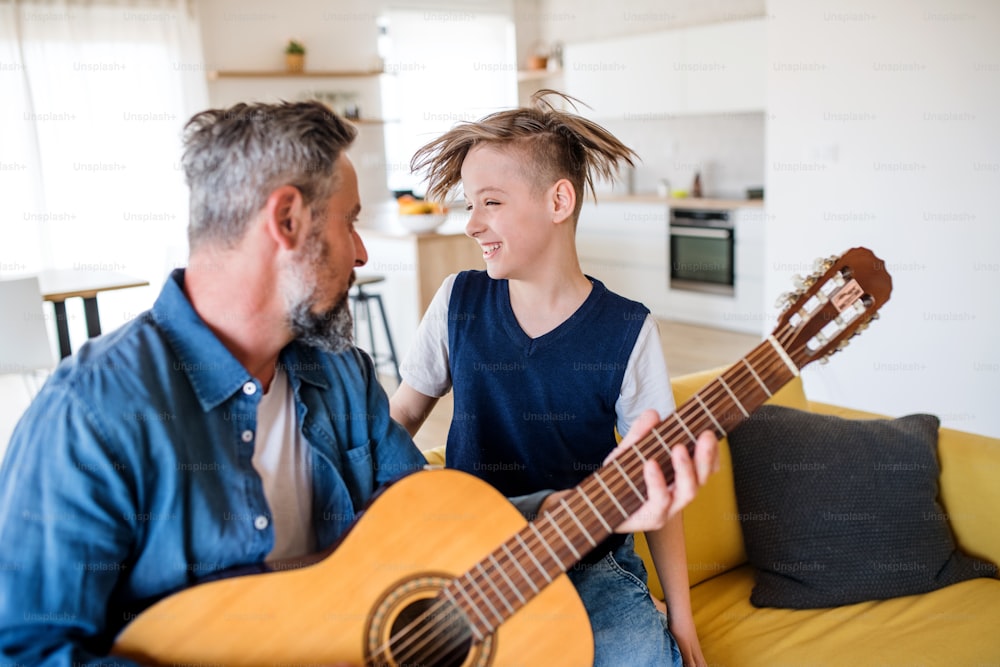 A mature father with small son sitting on sofa indoors, playing guitar.